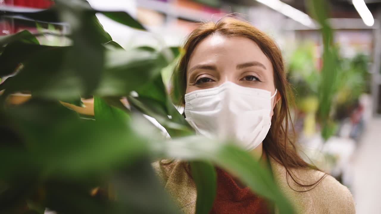красивая девушка в защитной медицинской маске и модной одежде смотрит в камеру за растениями