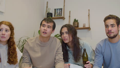 amigos emocionados viendo un partido de fútbol en la televisión en un momento crítico