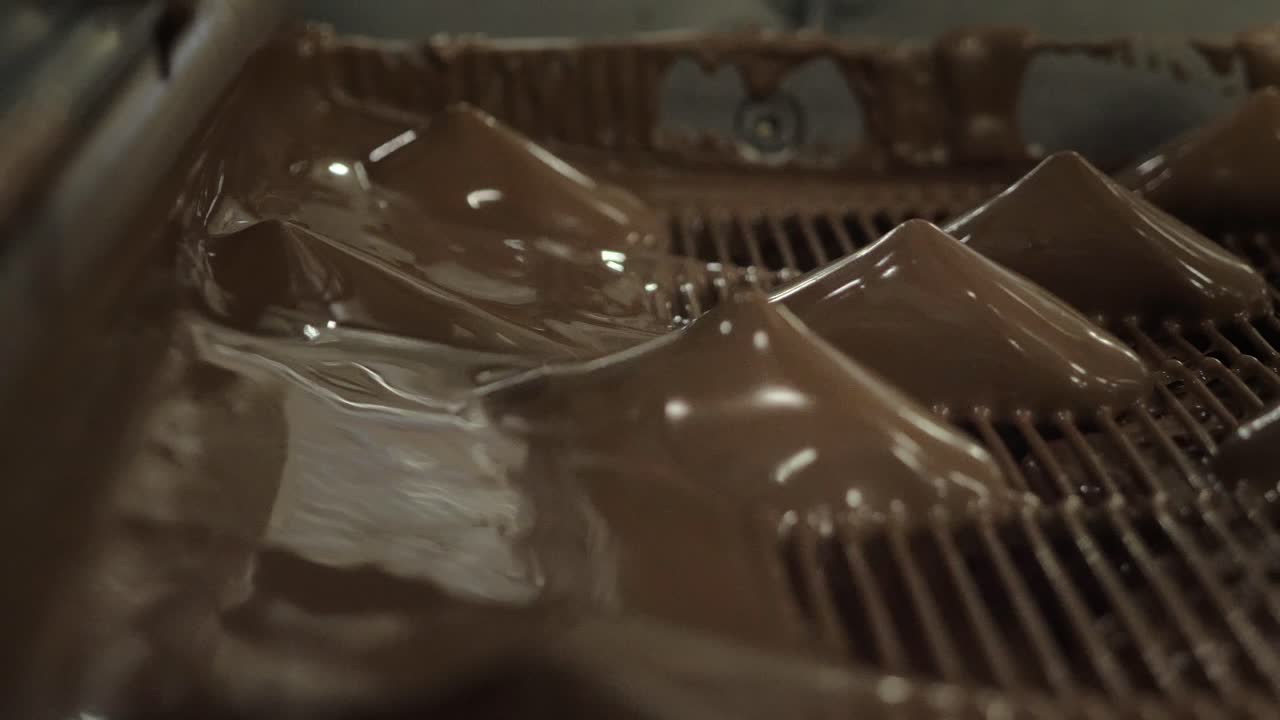 Close-up of candies being enrobed in flowing melted chocolate on a factory production line