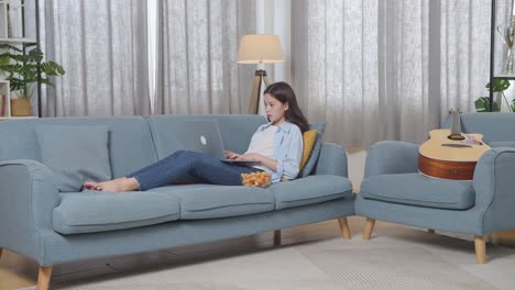 mujer trabajando en una computadora portátil en el sofá en casa con guitarra y bocadillo