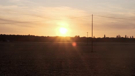 Establecimiento-De-Una-Toma-De-Campos-En-Primer-Plano-Cuando-Cae-La-Noche-En-Un-Telón-De-Fondo-De-Una-Puesta-De-Sol-Naranja-En-Normandía,-Francia