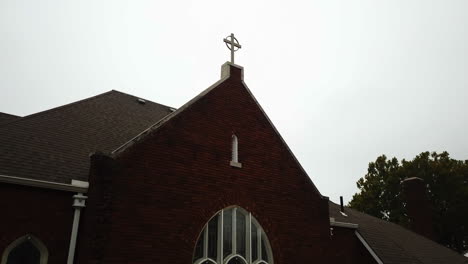 descending shot of a cross ontop of a church revealing the church