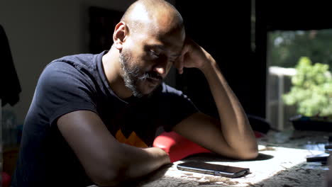 A casually dressed Asian man focused staring at his mobile phone on a counter table, the man waiting to receive an important call while anxiously swaying back and forth