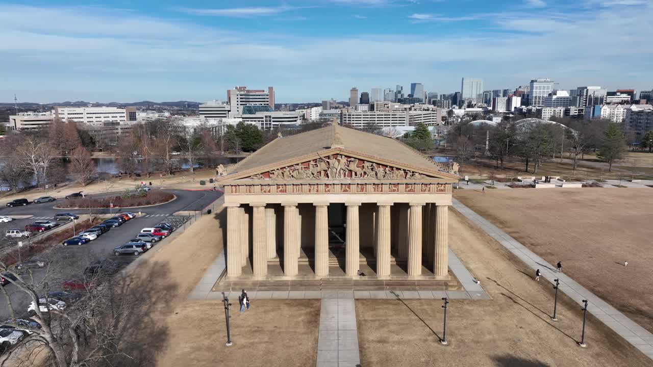 Vista aerea con drone del Partenone a Nashville, Tennessee, con lo skyline del centro che si staglia sullo sfondo, mostrando il Centennial Park e l'architettura moderna della città in una giornata limpida. Panoramica.