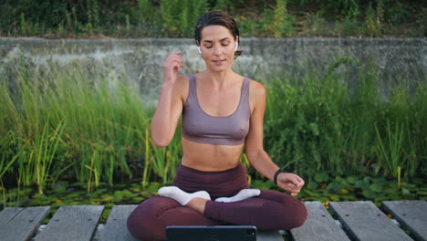 entrenador de yoga hablando lección sentado en la postura del loto banco. mujer insertando auricular