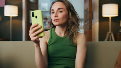 Young-lady-videocalling-telephone-sofa-interior-closeup.-Smiling-woman-gossiping