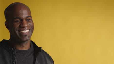 head and shoulders studio portrait of smiling and laughing mature man against yellow background