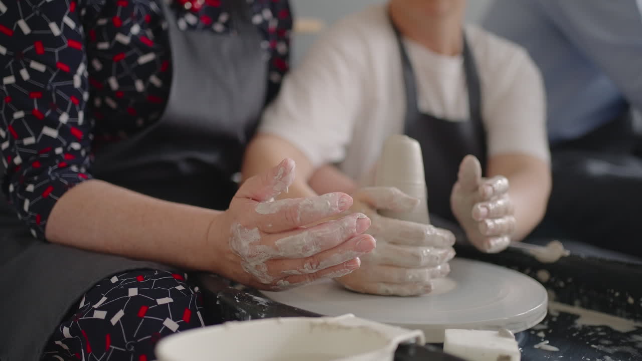 A female master shares her skills while giving a lesson for the elderly. Show grandmother the technique of working on a potter's wheel with ceramic clay