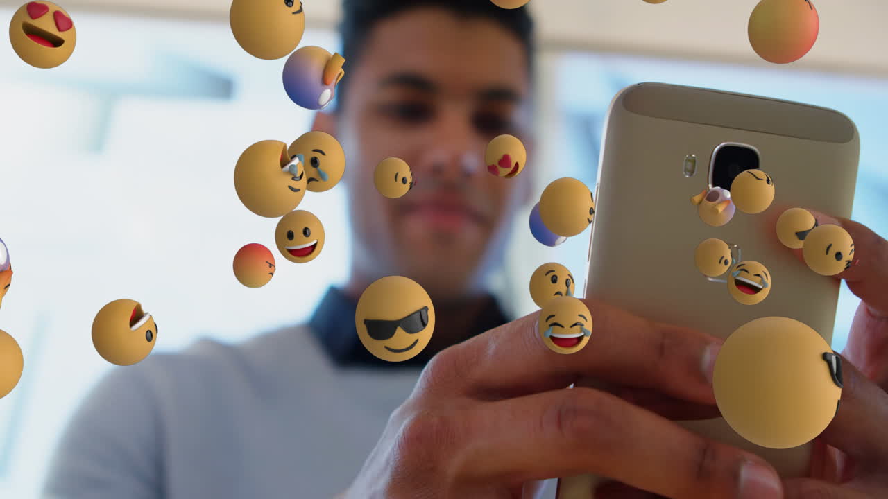 animación de varios emojis de cara flotando sobre un hombre biracial que usa un teléfono inteligente en la oficina
