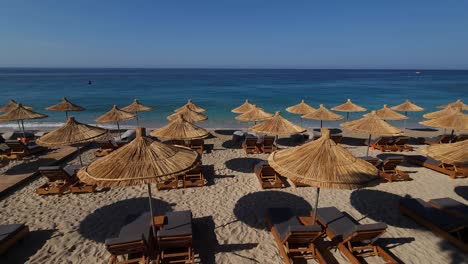 Wunderschöner-Strand-Mit-Sonnenschirmen-Und-Liegen-Auf-Sand,-Der-Bei-Sonnenaufgang-Am-Morgen-Von-Meereswellen-In-Albanien,-Ionische-Riviera,-Umspült-Wird