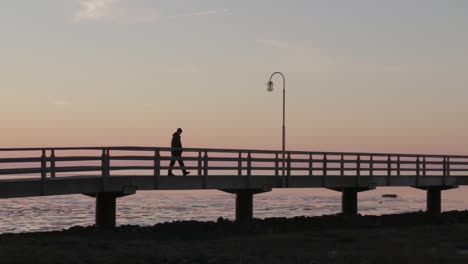 man walks on a bridge to an old antique lighthouse at the north sea while sunset