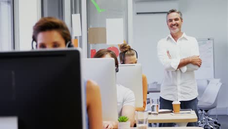 Smiling-executive-standing-with-arms-crossed-while-colleagues-talking-on-headset-4k