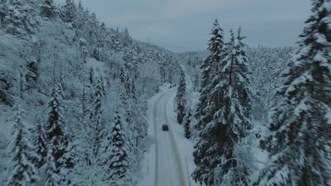 drone footage of an electric car driving in beautiful snowy landscape in norway with snow covered tree tops