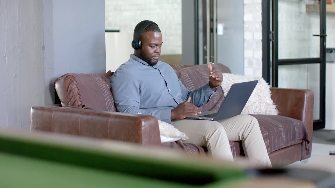 Happy african american casual businessman having laptop video call on couch in office, slow motion