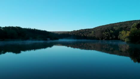 early morning low drone shot over glossy lake and some fog