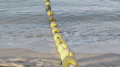 a close up shot of a line of yellow floating sea buoys being pushed around by small waves on the shoreline in pattaya, thailand