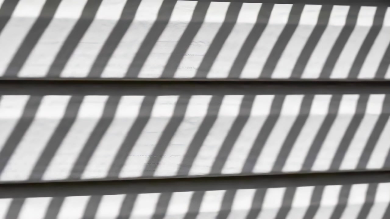 Sunlight casting diagonal shadow bands across horizontal lap siding on outdoor wall, hidden slats