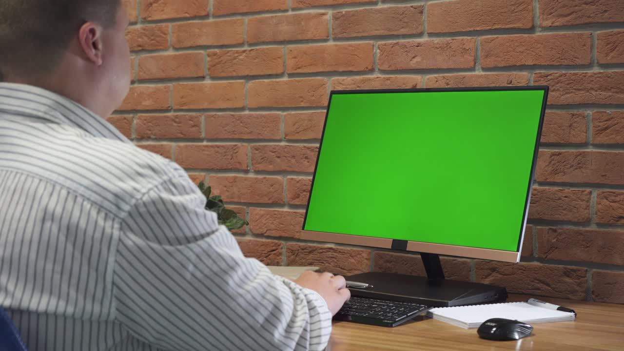 남자는 사무실에서 녹색 모의 화면으로 개인 컴퓨터에서 일합니다.