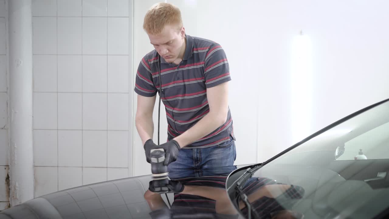 trabajador rojo está procesando la superficie del coche con una máquina de pulido en un servicio de automóviles, cubriendo con una capa protectora