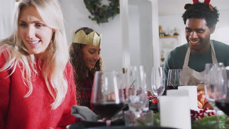 Family-Playing-With-Christmas-Cracker-Novelties-As-They-Sit-For-Meal-At-Table