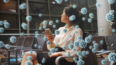 animation of floating macro covid-19 cells over biracial woman using smartphone at airport