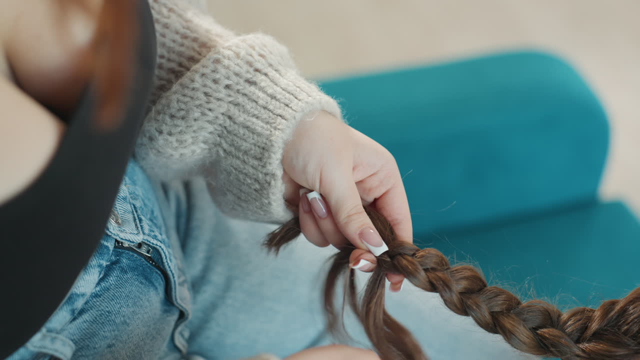 Caucasian Hands Weaving Thick Braid Near Teal Chair Apprentice Stylist Securing Elastic And Smoothing Ends, Knit Sweater Sleeve, Focused Fingers, Clean Manicure, StepByStep Technique, Calm