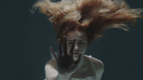 beautiful redhaired girl stopped underwater in front of the camera and froze