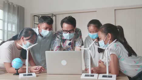 wearing facemasks, enthusiastic asian teacher explains to young children how wind turbines work. kids learning about eco-friendly forms of renewable energy