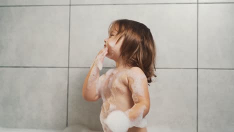 a cute two-year-old girl is playing with bath foam