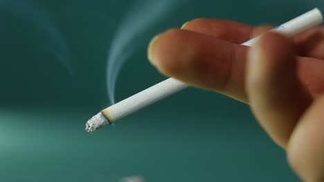 Closeup-shot-of-a-hand-holding-a-lit-cigarette,-with-smoke-trailing-from-the-cigarette,-stop-smoking-message