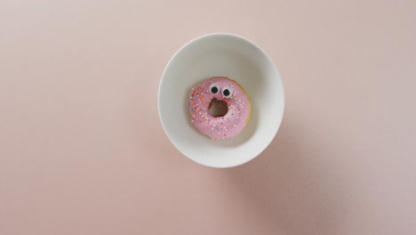 video of donut with icing on white plate over pink background