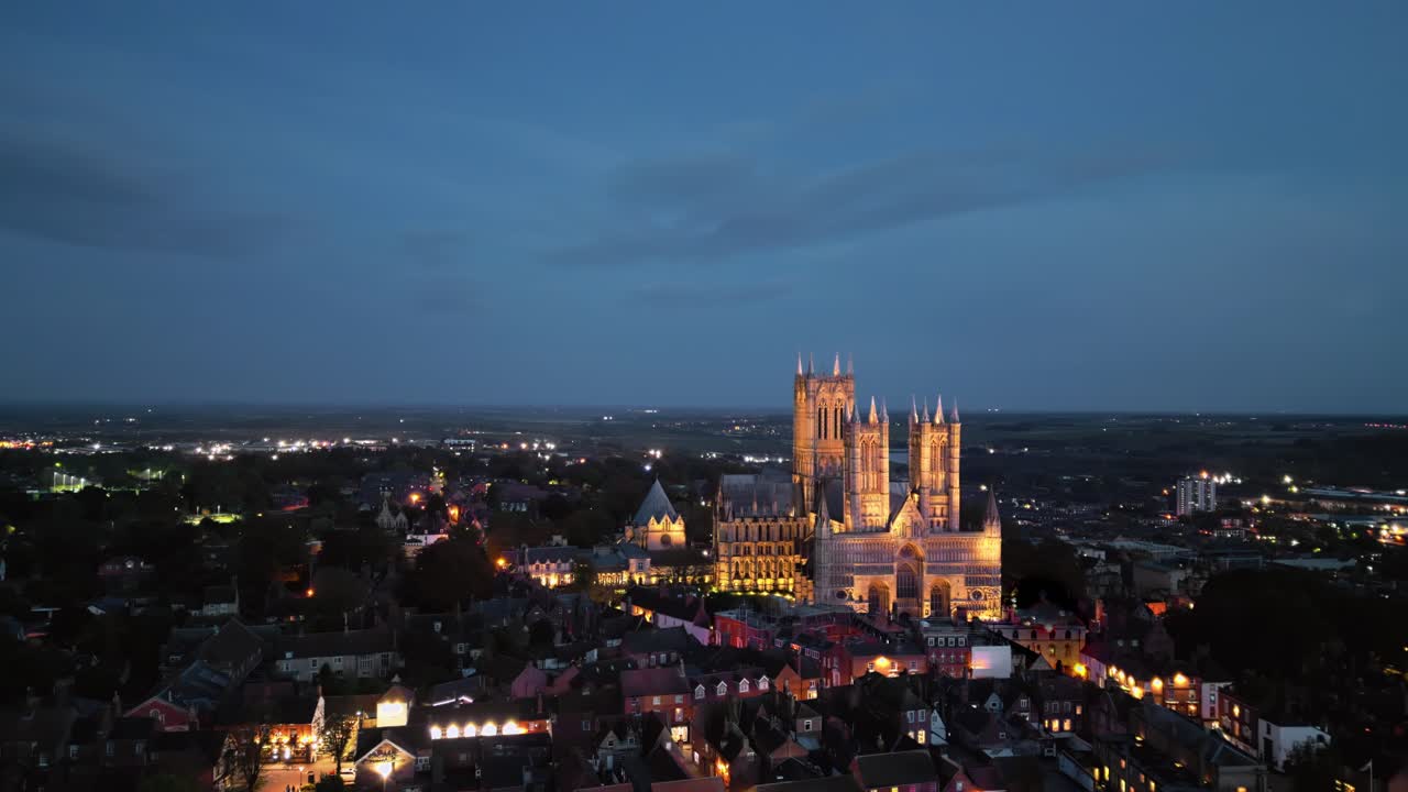 Vídeo aéreo de drone captura a renomada Catedral de Lincoln em Lincolnshire, Reino Unido, ao anoitecer, exibindo sua majestosa arquitetura gótica com iluminação