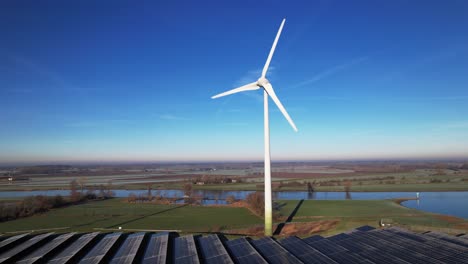 gefrorene sonnenkollektoren vor einer einsamen windkraftanlage, teil einer nachhaltigen industrie in einer flachen flusslandschaft in den niederlanden vor blauem himmel