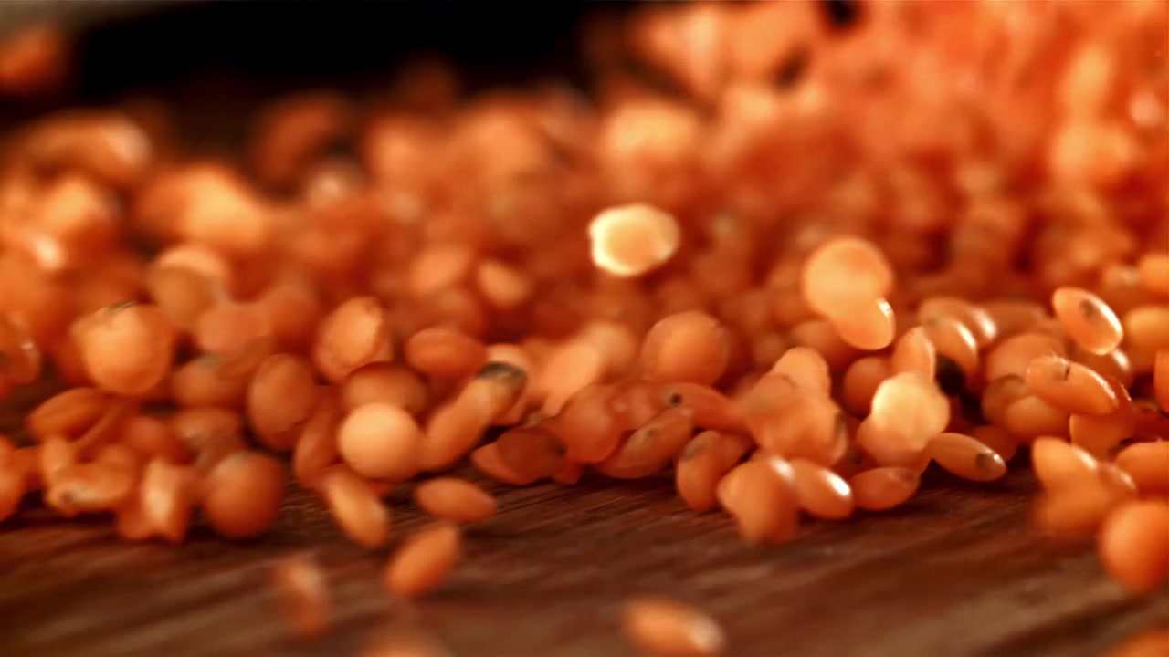 Lenticchie rosse che cadono e si disperdono su una superficie di legno al rallentatore