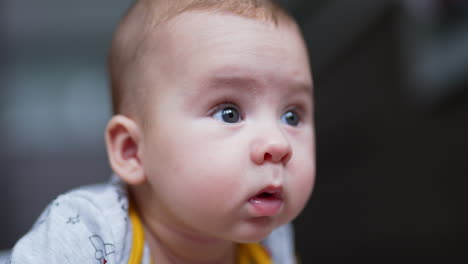 beautiful face of a small caucasian infant boy lying on his belly. cute baby looking around with surprise. close up. blurred backdrop.