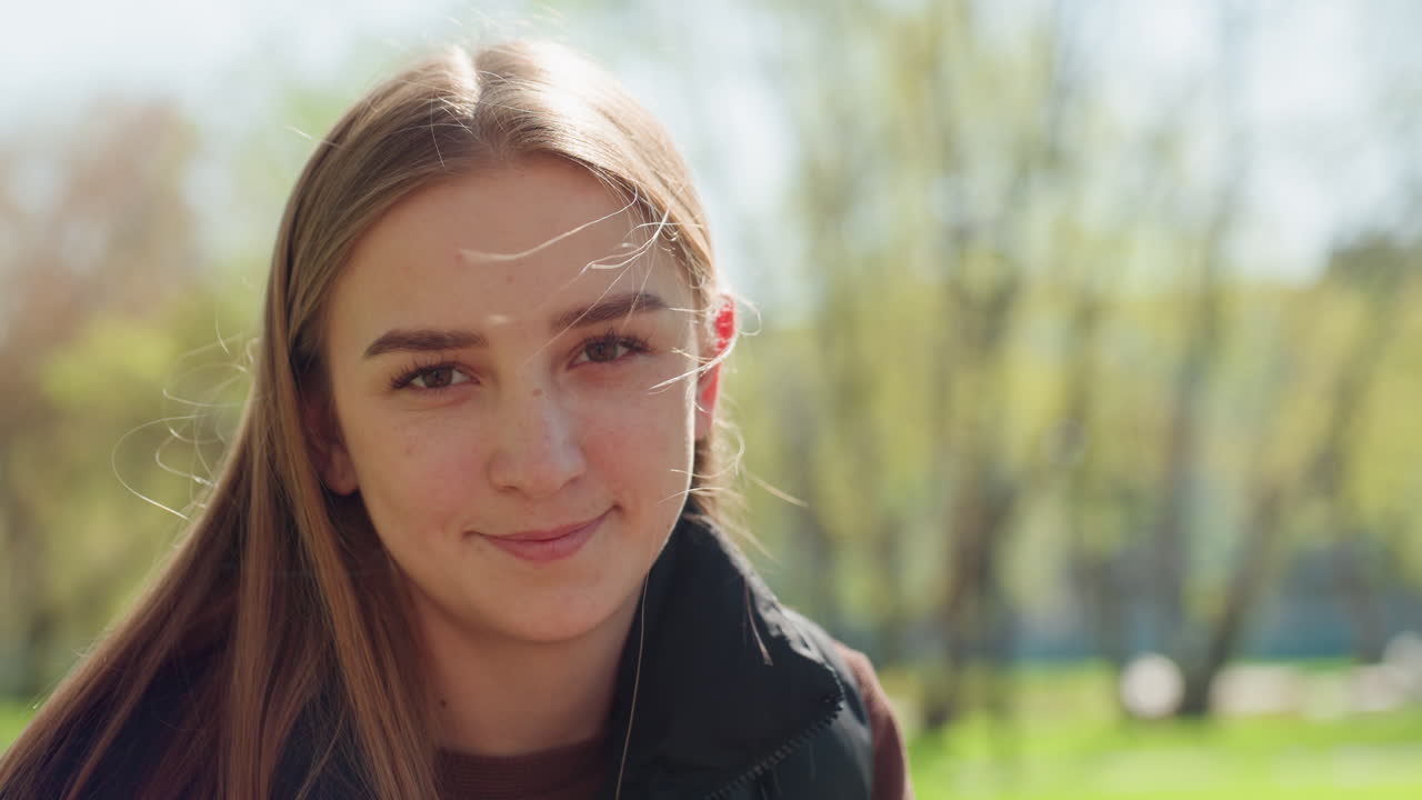 Una adolescente tejiendo en un parque soleado, escuchando música con auriculares, primer plano enfocado en las manos y las agujas, fondo bokeh suave con vegetación y luz cálida de primavera, escena tranquila de un pasatiempo consciente
