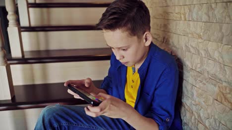concentrated in games on phone boy sitting on stairs. teenager in casual clothing sitting at home on staircase and having fun playing on a cell phone.