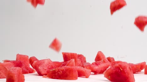 Rosafarbene,-Saftige-Wassermelonenwürfel,-Die-In-Zeitlupe-Auf-Die-Weiße-Tischplatte-Fallen-Und-Hüpfen,-Wobei-überall-Saft-Und-Samen-Spritzen