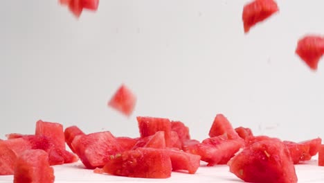 pink, juicy diced watermelon cube pieces falling and bouncing on white table top in slow motion with juice and seeds splattering everywhere