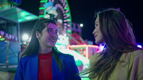 joyful girls walking amusement park at night closeup. happy best friends laugh