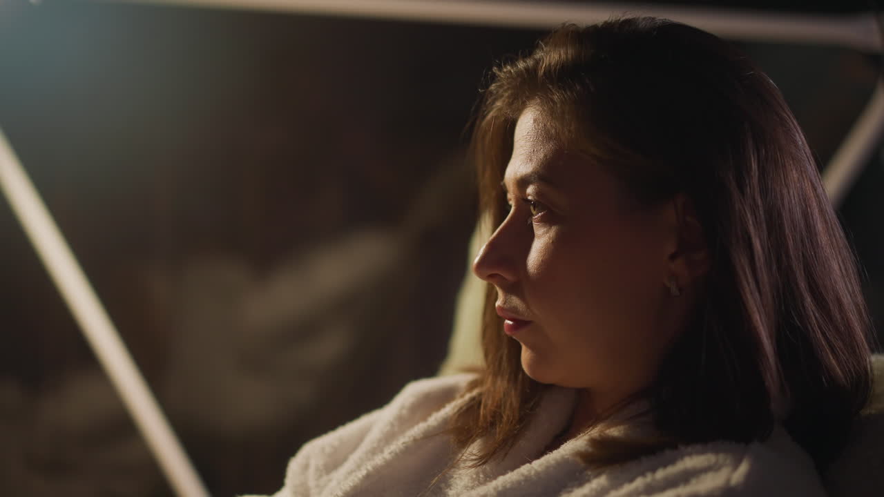 Lady suffers from depressive thoughts relaxing in dimly lit hotel room. Woman immersed in thoughts gazes at wide window. Video depicts concept of loneliness