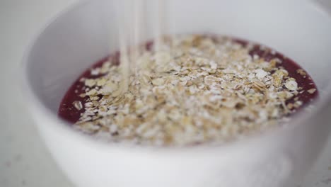 sprinkling oats on top of red berry smoothie in white ceramic bowl