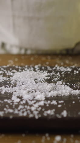 chef throws fat pickled herring into salt pile on wooden cutting board in kitchen close view. healthy nutrition of seafood products