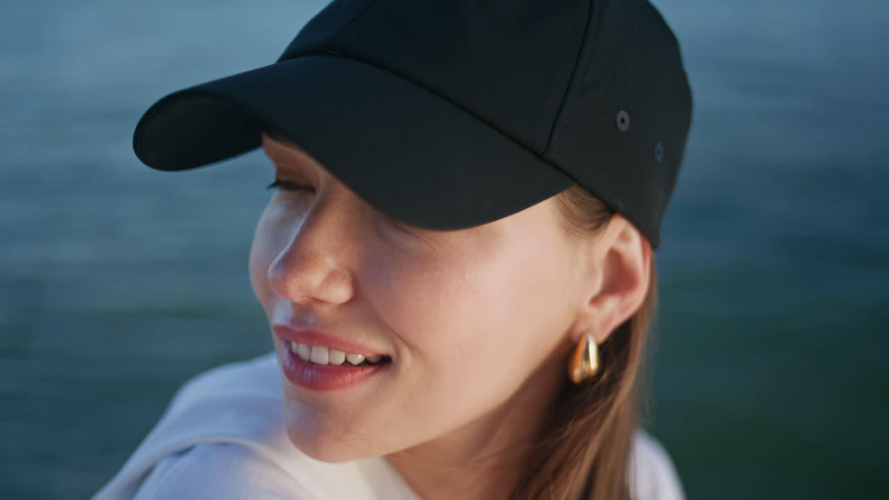 Portrait woman relaxing at waterfront wearing black cap. Carefree lady