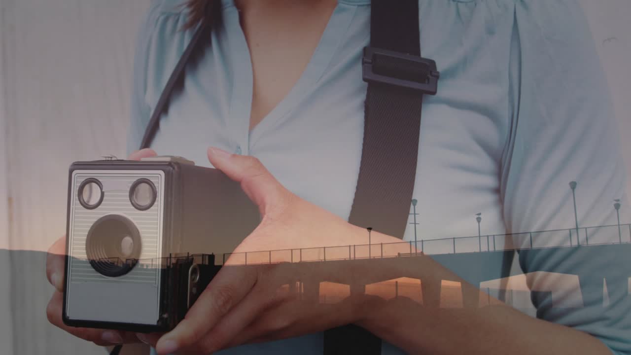 Woman raising vintage camera and turning winding knob for education showing sunset pier overlay