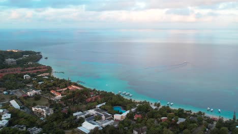 cinematic aerial view of caribbean coast with boats, turquoise water, beach, resorts during sunrise, island background, roatan island,west end, honduras