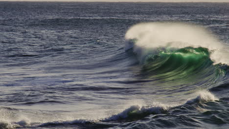 telephoto static super slow motion backdrop of ocean wave glistening green illuminated as mist rises off back