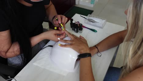 anonymous ethnic doing manicure to client and applying nail polish