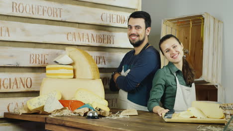 Successful-Small-Business-The-Man-And-The-Woman-Behind-The-Counter-Of-The-Store-Cheeses-Looking-At-C