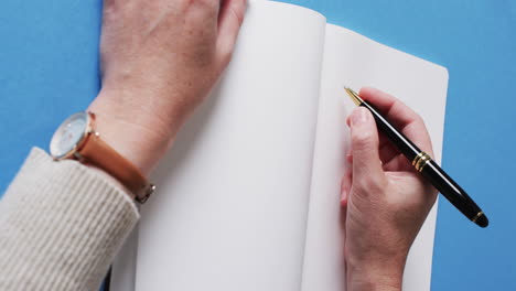 close up of hand writing with pen on book with copy space on blue background in slow motion